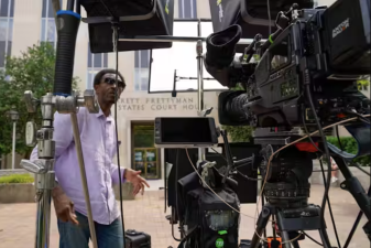 An image of a man with multiple cameras and other equipment.